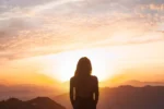 photo of a person looking at the sunrise in the mountains, symbolizing spiritual awakening and inner connection.