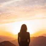 photo of a person looking at the sunrise in the mountains, symbolizing spiritual awakening and inner connection.