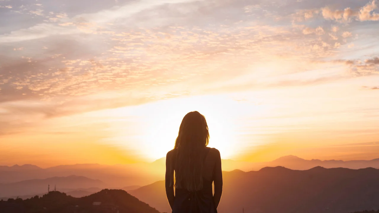 photo of a person looking at the sunrise in the mountains, symbolizing spiritual awakening and inner connection.
