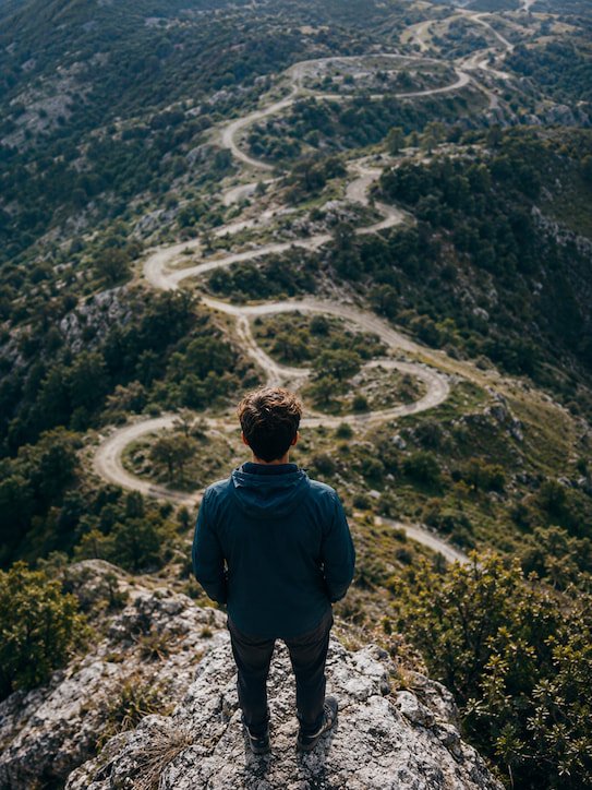 Nonlinear Awakening Person overlooking a winding mountain road, representing the nonlinear stages of spiritual awakening.